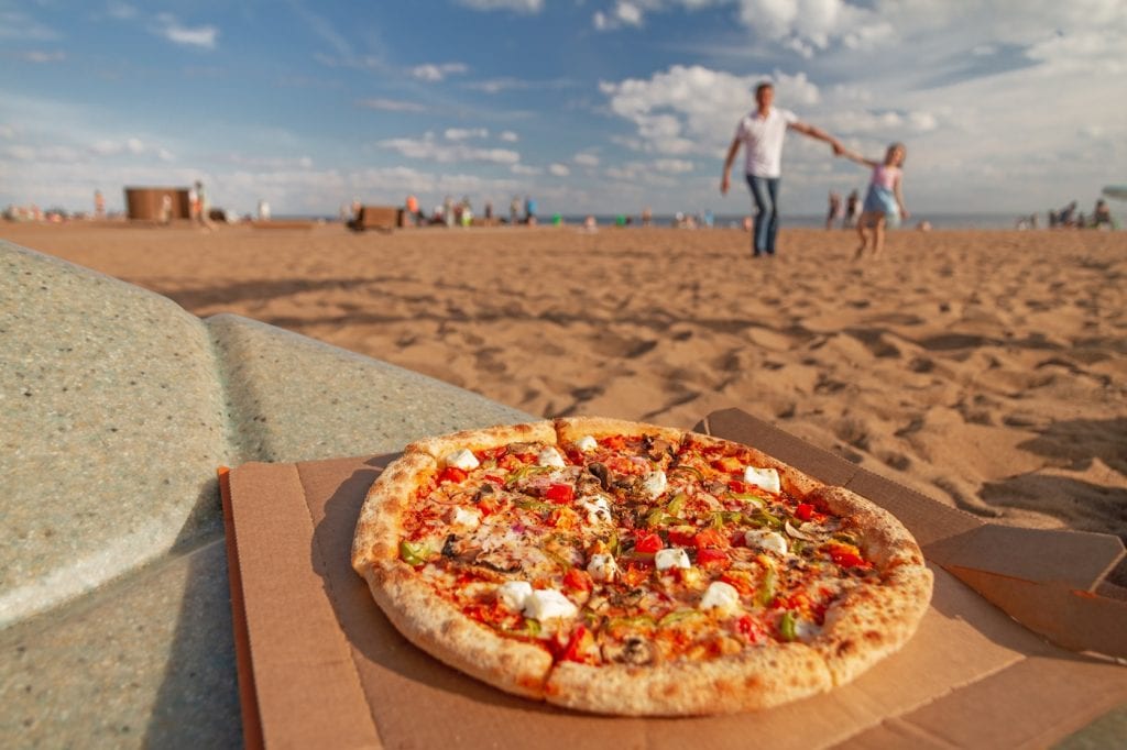 pizza lies on table in far background happy dad and daughter play in sand in blur on beach